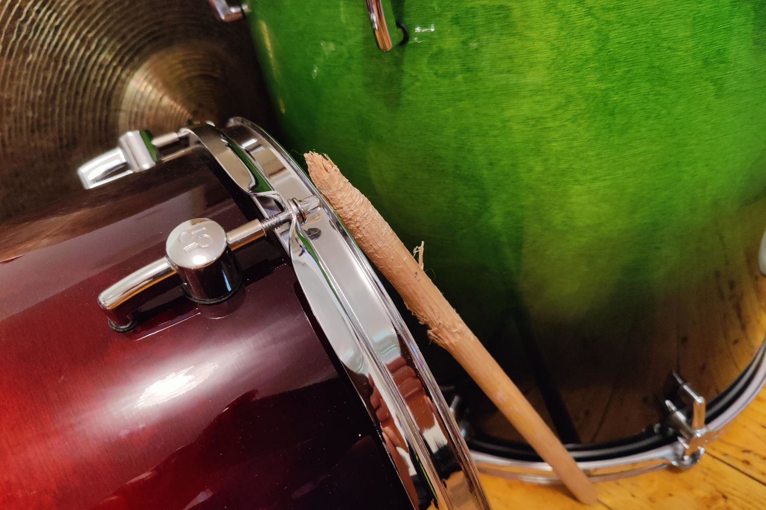 A red and a green drum shell. A heavily used drumstick is leaning against them.